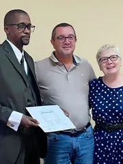 Gros plan sur M. ITOUA-NDZANGA tenant fièrement son diplôme du concours d'écriture 2025 aux côtés des membres du jury.