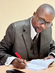 M. ITOUA-NDZANGA en train de dédicacer un exemplaire de son ouvrage avec un stylo rouge lors de la cérémonie de remise des prix.